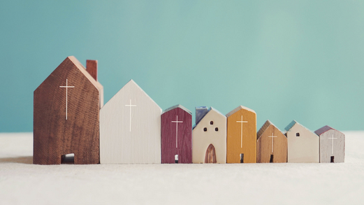 Acht kleine Holzkirchen in verschiedenen Größen und Farben stehen nebeneinander.