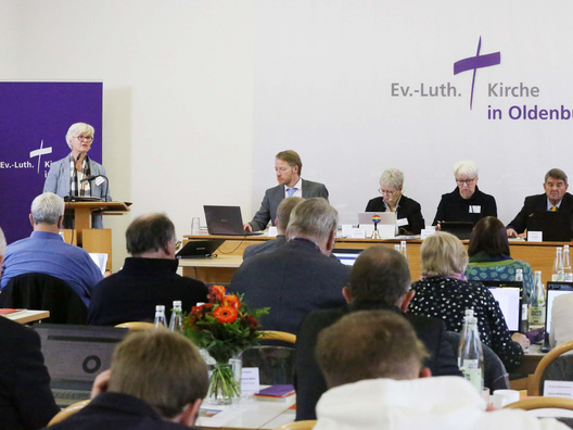 Oberkirchenrätin Gudrun Mawick steht am Rednerpult. Das Plenum ist von hinten zu sehen.