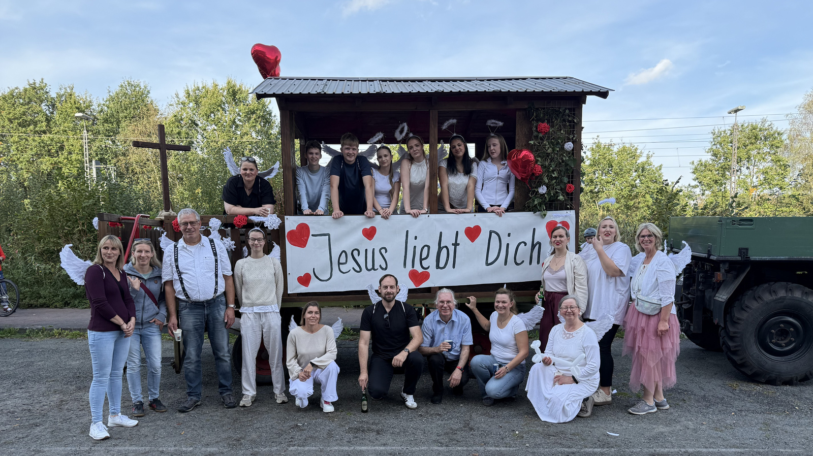 Gruppenfoto aller Beteiligten am Erntedank-Umzug vor dem Festwagen bei blauem Himmel.