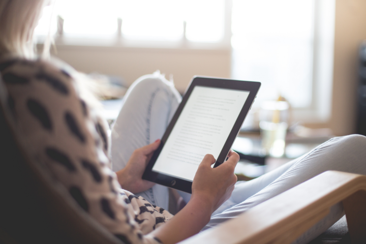 Eine Frau sitzt gemütlich auf einem Sessel und liest auf einem Tablet.