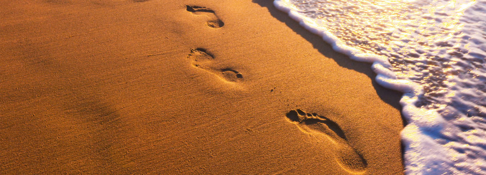 Sandstrand mit Spuren im Sand. Rechts daneben auslaufende Wellen des Meeres.