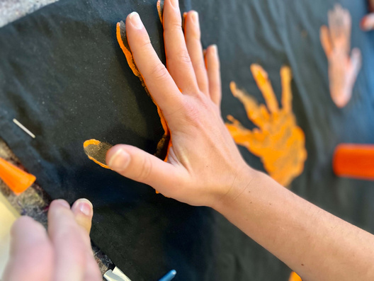 Eine Hand druckt mit Farbe auf ein schwarzes Laken.