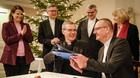 Bischof Dr. Heiner Wilmer, Bistum Hildesheim (links), und Bischof Thomas Adomeit, Ratsvorsitzender der Konföderation evangelischer Kirchen in Niedersachsen (rechts), tauschen die unterschriebene Vereinbarung zum neuen Unterrichtsfach Christliche Religion aus. Links daneben steht die niedersächsische Kultusministerin Julia Willie Hamburg. 