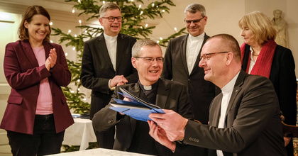 Bischof Dr. Heiner Wilmer, Bistum Hildesheim (links), und Bischof Thomas Adomeit, Ratsvorsitzender der Konföderation evangelischer Kirchen in Niedersachsen (rechts), tauschen die unterschriebene Vereinbarung zum neuen Unterrichtsfach Christliche Religion aus. Links daneben steht die niedersächsische Kultusministerin Julia Willie Hamburg. 