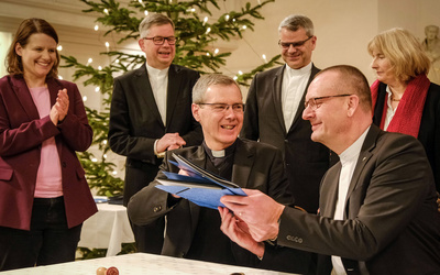 Bischof Dr. Heiner Wilmer, Bistum Hildesheim (links), und Bischof Thomas Adomeit, Ratsvorsitzender der Konföderation evangelischer Kirchen in Niedersachsen (rechts), tauschen die unterschriebene Vereinbarung zum neuen Unterrichtsfach Christliche Religion aus. Links daneben steht die niedersächsische Kultusministerin Julia Willie Hamburg. 